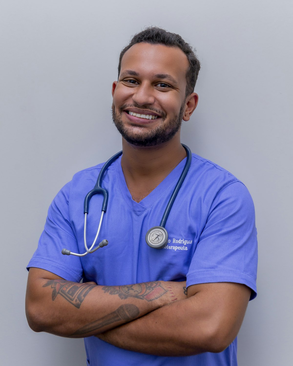 A smiling nurse in scrubs with a stethoscope, arms crossed